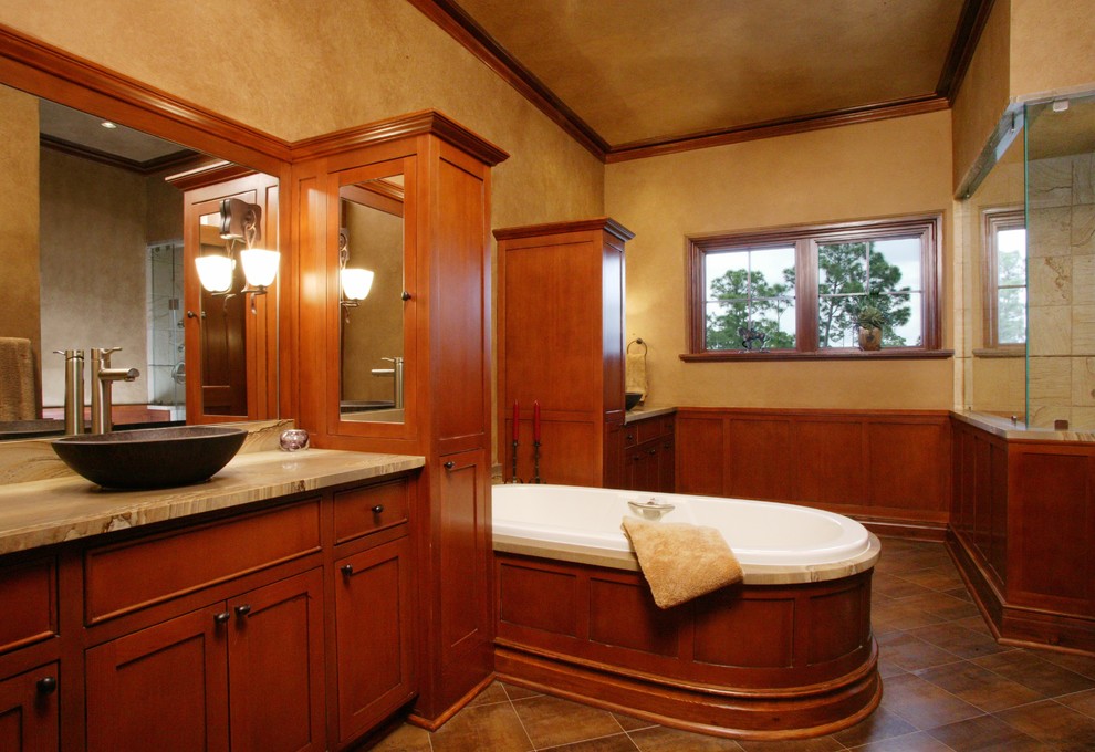 Mediterranean master bathroom in Minneapolis with a vessel sink, recessed-panel cabinets, medium wood cabinets, granite benchtops, a freestanding tub, an alcove shower, a one-piece toilet, brown tile, stone tile, brown walls and travertine floors.