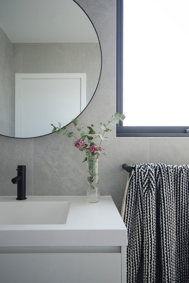This is an example of a mid-sized modern 3/4 bathroom in Canberra - Queanbeyan with furniture-like cabinets, an open shower, a one-piece toilet, gray tile, porcelain tile, grey walls, porcelain floors, an integrated sink, solid surface benchtops, grey floor, an open shower, white benchtops, a niche and a floating vanity.