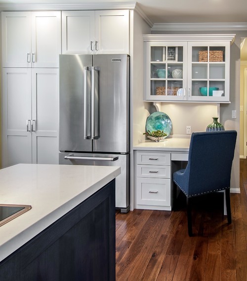 Bright kitchen corner with white shaker cabinets, stainless steel fridge, glass-front display cabinet, and built-in desk nook — Kitchen Cabinet Mississauga.