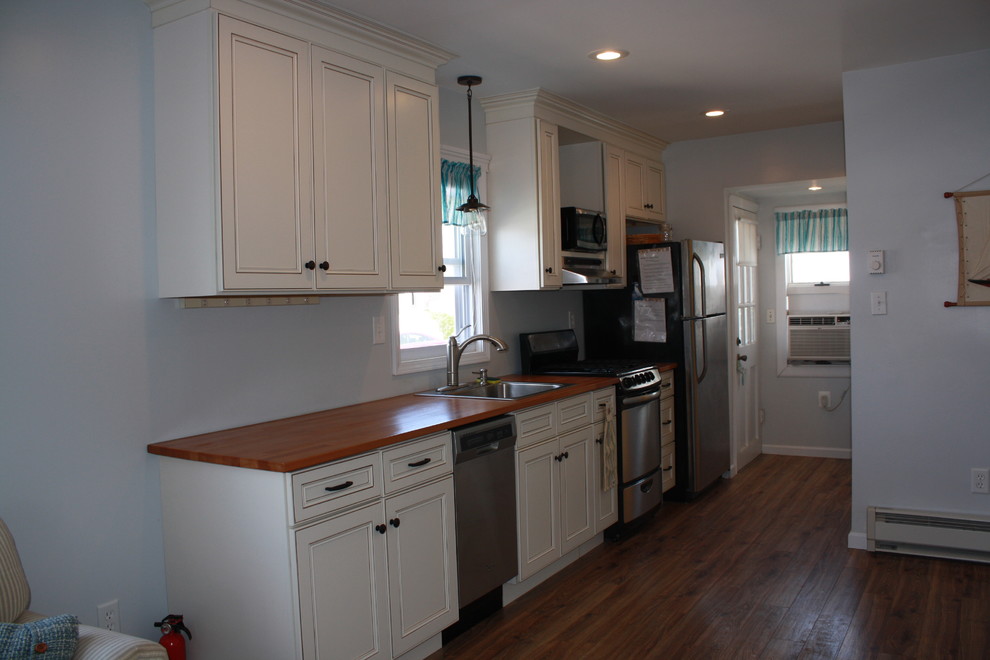 Photo of a small beach style single-wall open plan kitchen in Philadelphia with a drop-in sink, flat-panel cabinets, white cabinets, wood benchtops, stainless steel appliances, medium hardwood floors and no island.