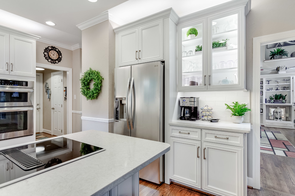 Mid-sized transitional u-shaped medium tone wood floor and brown floor eat-in kitchen photo in Birmingham with a double-bowl sink, recessed-panel cabinets, white cabinets, quartz countertops, white backsplash, subway tile backsplash, stainless steel appliances, a peninsula and white countertops