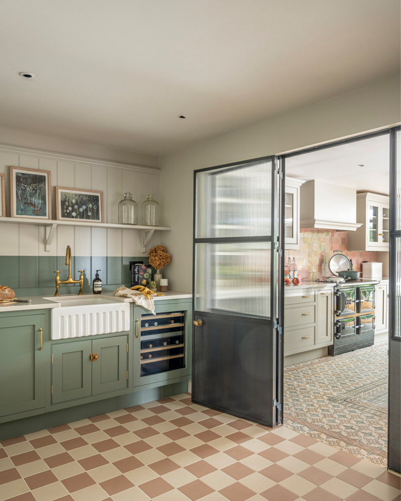 Inspiration for a traditional kitchen/diner in Buckinghamshire with a belfast sink, shaker cabinets, green cabinets, composite countertops, pink splashback, ceramic splashback, black appliances, ceramic flooring, an island and white worktops.