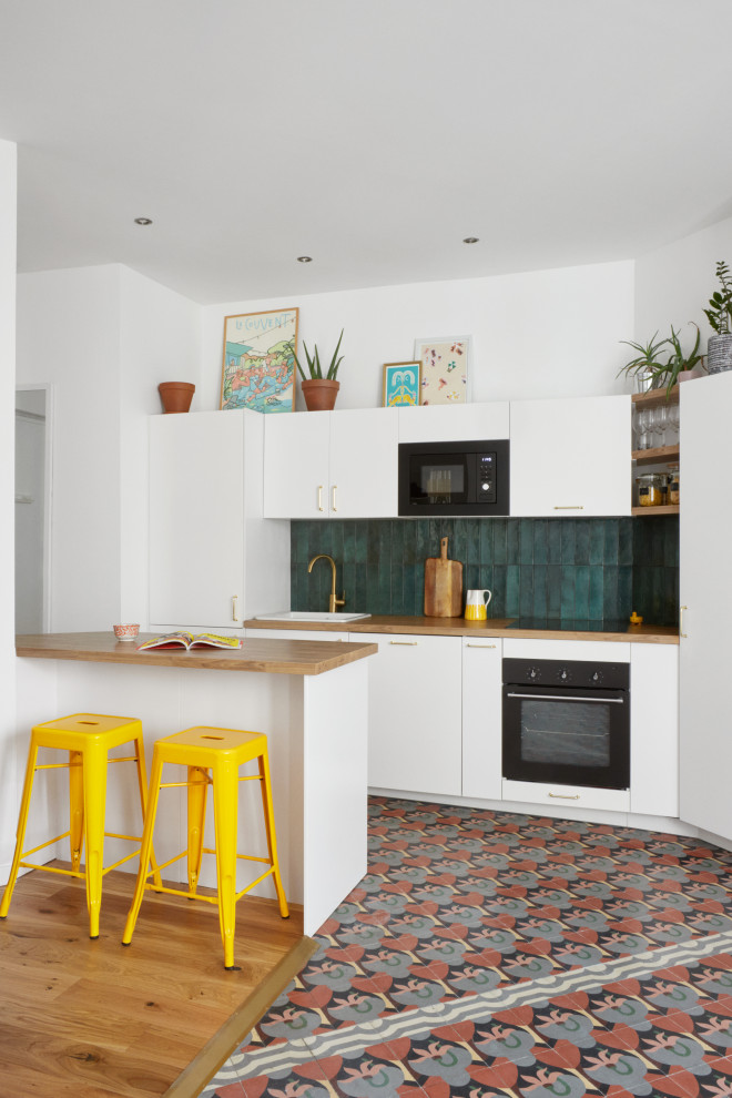 Photo of a contemporary l-shaped kitchen in Marseille with a built-in sink, flat-panel cabinets, white cabinets, wood worktops, green splashback, black appliances, an island, multi-coloured floors and beige worktops.