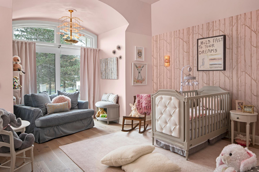 Photo of a traditional nursery for girls in Detroit with pink walls and light hardwood floors.