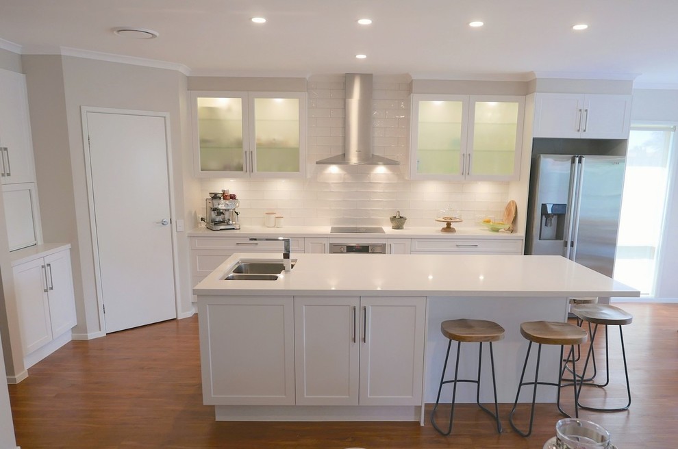 Photo of a mid-sized beach style galley kitchen pantry in Brisbane with an undermount sink, shaker cabinets, white cabinets, quartz benchtops, white splashback, subway tile splashback, stainless steel appliances, laminate floors and with island.