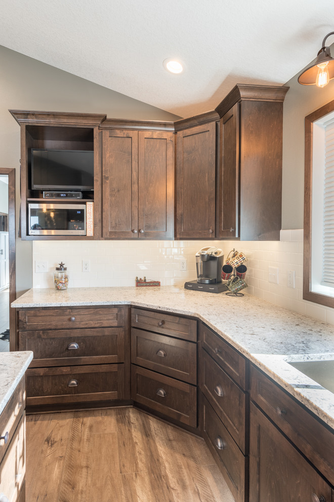 This is an example of a large country u-shaped separate kitchen in Minneapolis with a double-bowl sink, shaker cabinets, dark wood cabinets, granite benchtops, white splashback, subway tile splashback, stainless steel appliances, dark hardwood floors, with island and brown floor.