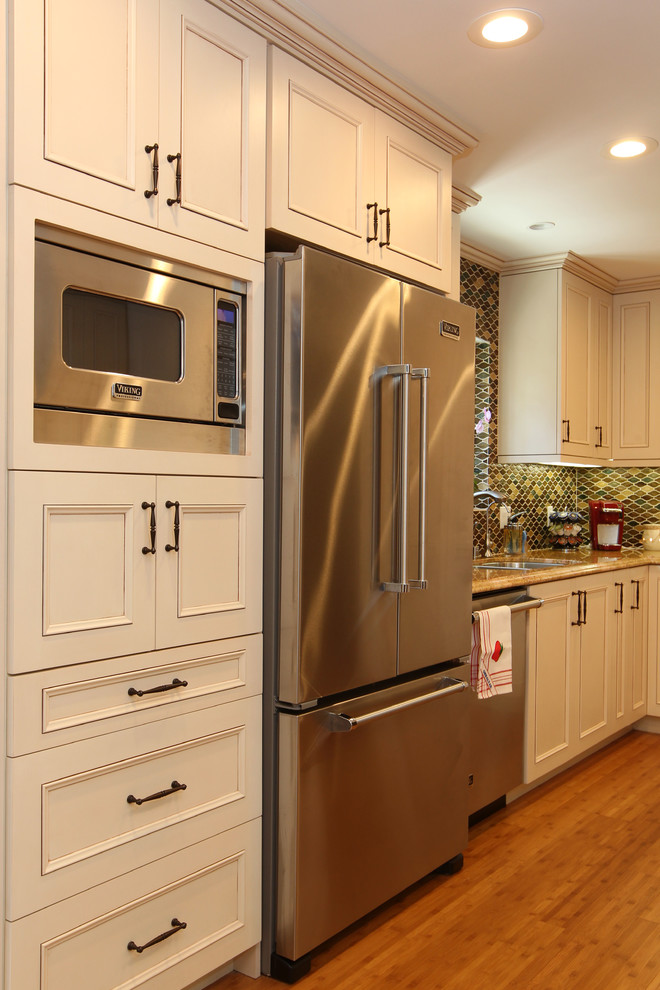 This is an example of a mid-sized traditional u-shaped eat-in kitchen in Los Angeles with an undermount sink, recessed-panel cabinets, beige cabinets, granite benchtops, multi-coloured splashback, glass tile splashback, stainless steel appliances, bamboo floors, no island and beige floor.