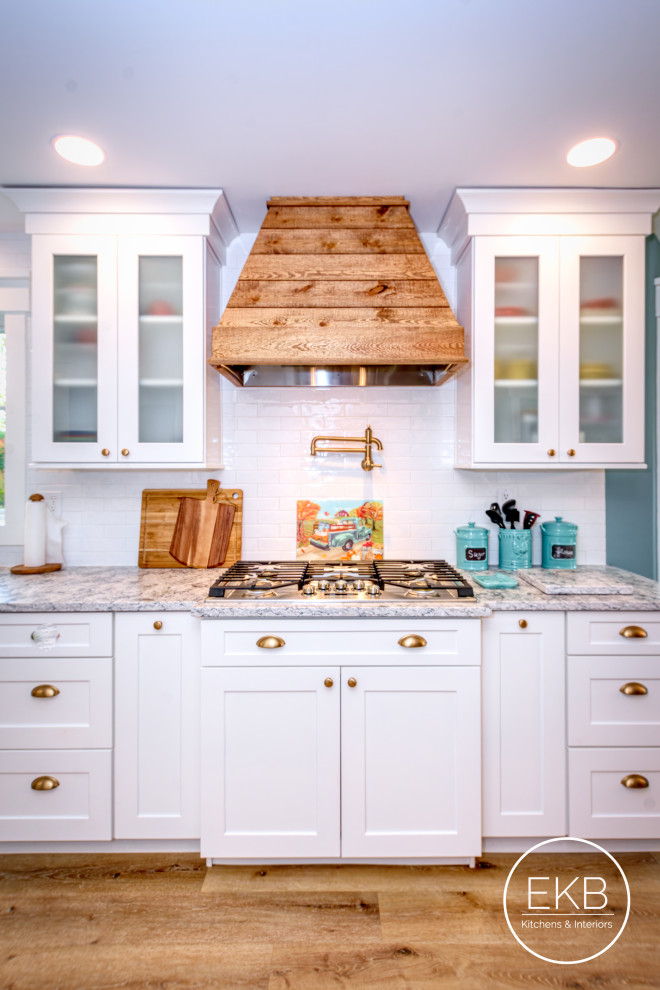Inspiration for a large transitional single-wall eat-in kitchen in New York with a farmhouse sink, shaker cabinets, white cabinets, granite benchtops, white splashback, ceramic splashback, stainless steel appliances, light hardwood floors, a peninsula and multi-coloured benchtop.