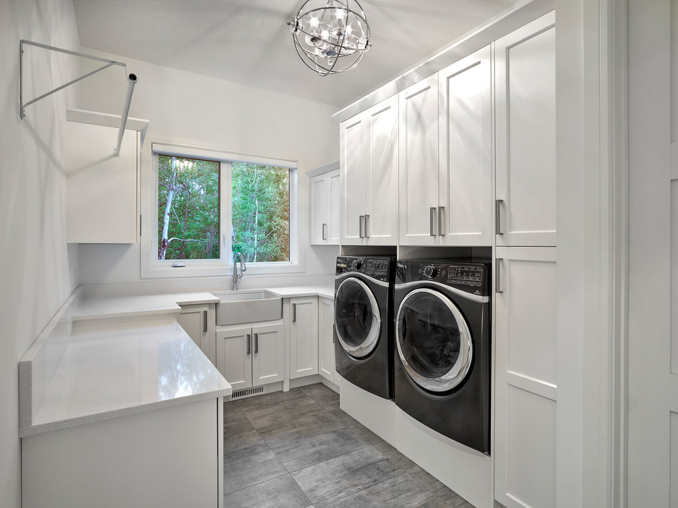 Mid-sized modern u-shaped utility room in Edmonton with a farmhouse sink, shaker cabinets, white cabinets, white walls and a side-by-side washer and dryer.