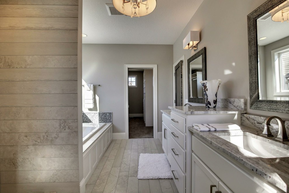 This is an example of a large transitional master bathroom in Minneapolis with shaker cabinets, white cabinets, a drop-in tub, an alcove shower, a one-piece toilet, black tile, gray tile, white tile, mosaic tile, grey walls, porcelain floors, an undermount sink and granite benchtops.