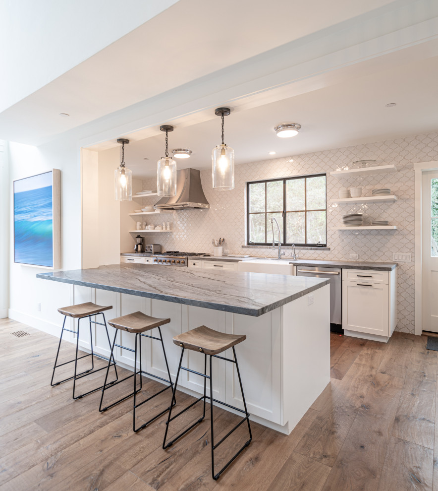 Inspiration for a mid-sized transitional galley open plan kitchen in Santa Barbara with medium hardwood floors, brown floor, timber, a farmhouse sink, shaker cabinets, white cabinets, white splashback, stainless steel appliances, a peninsula and grey benchtop.