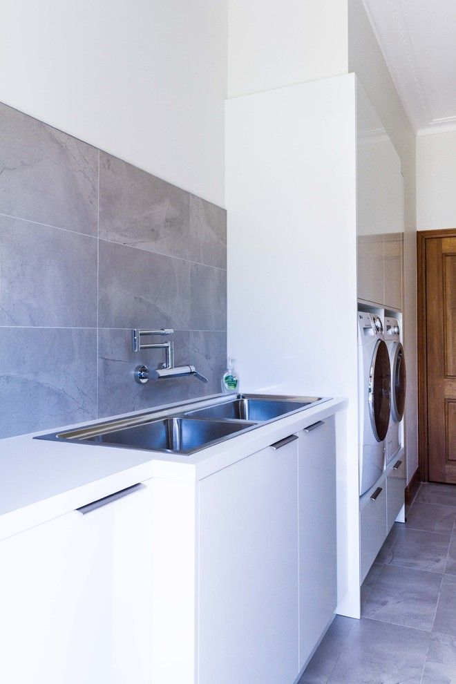 This is an example of a mid-sized contemporary galley dedicated laundry room in Melbourne with flat-panel cabinets, white cabinets, laminate benchtops, white walls, porcelain floors and a side-by-side washer and dryer.