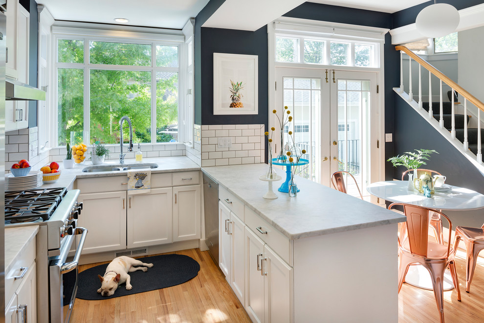 Inspiration for a transitional u-shaped eat-in kitchen in Minneapolis with a double-bowl sink, shaker cabinets, white cabinets, white splashback, subway tile splashback, stainless steel appliances, medium hardwood floors and a peninsula.