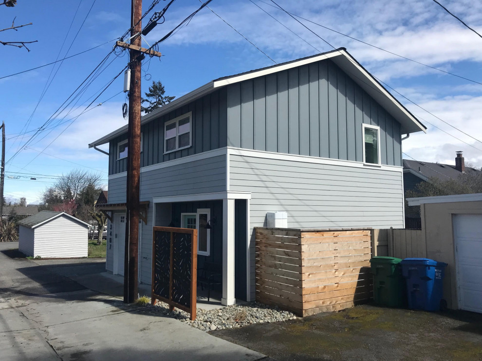 This is an example of a medium sized and gey contemporary two floor detached house in Seattle with concrete fibreboard cladding, a pitched roof, a shingle roof, a black roof and board and batten cladding.
