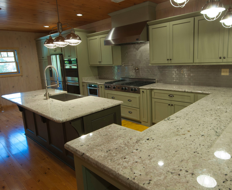 This is an example of a traditional u-shaped eat-in kitchen in Other with a farmhouse sink, shaker cabinets, green cabinets, granite benchtops, metallic splashback, subway tile splashback, stainless steel appliances and with island.