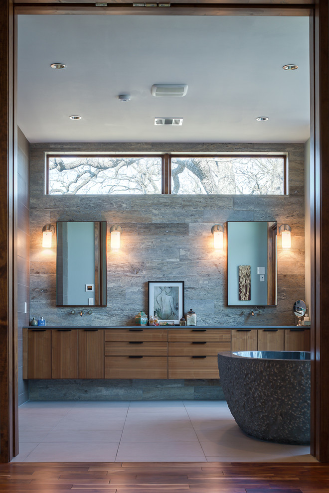This is an example of a large contemporary master bathroom in Austin with grey walls, porcelain floors, flat-panel cabinets, medium wood cabinets, a freestanding tub, an alcove shower, gray tile, porcelain tile, an undermount sink and engineered quartz benchtops.