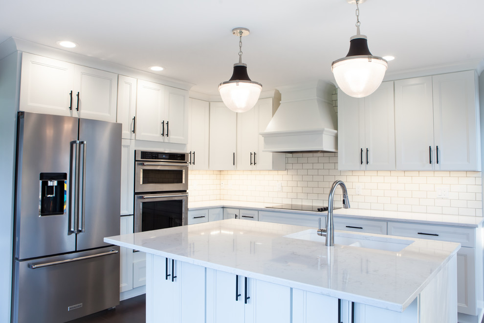 Large transitional l-shaped dark wood floor and brown floor eat-in kitchen photo with an undermount sink, recessed-panel cabinets, white cabinets, quartz countertops, white backsplash, subway tile backsplash, stainless steel appliances and an island