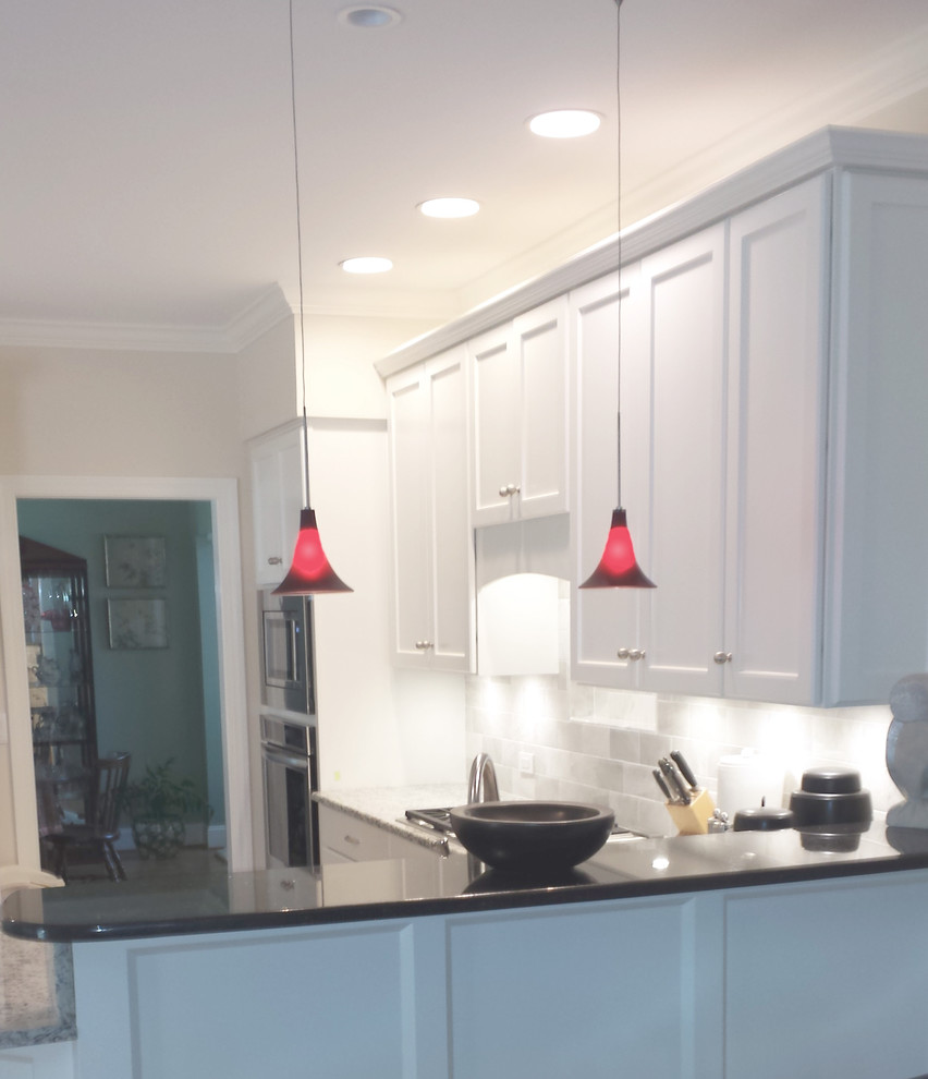 Inspiration for a huge transitional l-shaped light wood floor eat-in kitchen remodel with an undermount sink, recessed-panel cabinets, white cabinets, granite countertops, white backsplash, stone tile backsplash, white appliances and a peninsula
