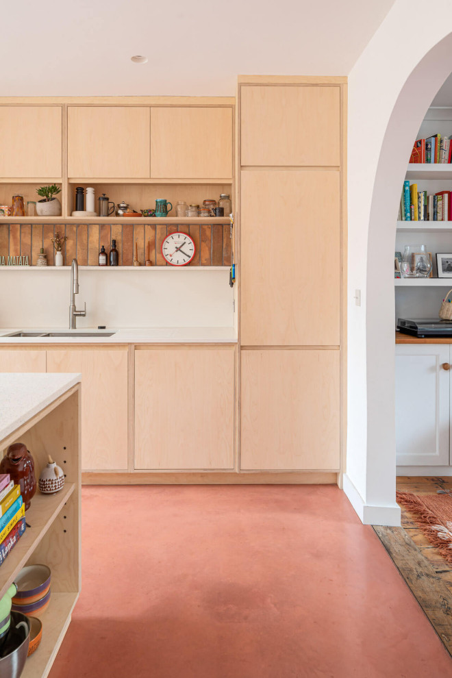Cette photo montre une grande cuisine ouverte parallèle tendance en bois clair avec un placard à porte plane, sol en béton ciré, îlot et un sol rose.