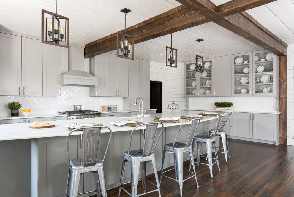 This is an example of a country l-shaped eat-in kitchen in Dallas with a farmhouse sink, shaker cabinets, grey cabinets, white splashback, stainless steel appliances, dark hardwood floors, with island and brown floor.