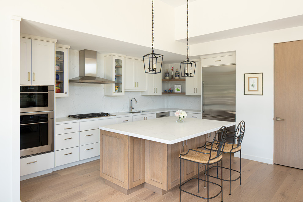Open concept kitchen - mid-sized transitional l-shaped light wood floor and beige floor open concept kitchen idea in Boise with a drop-in sink, shaker cabinets, white cabinets, marble countertops, white backsplash, marble backsplash, stainless steel appliances, an island and white countertops