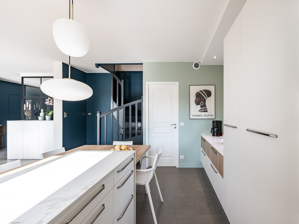 This is an example of a large scandinavian l-shaped open plan kitchen in Lyon with an integrated sink, flat-panel cabinets, white cabinets, marble benchtops, marble splashback, stainless steel appliances, ceramic floors, with island and grey floor.