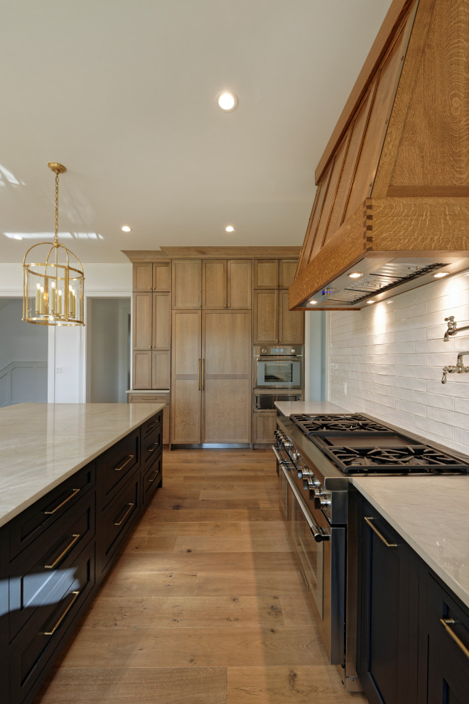 Idéer för stora amerikanska linjära flerfärgat kök och matrum, med en rustik diskho, luckor med profilerade fronter, bruna skåp, granitbänkskiva, vitt stänkskydd, stänkskydd i glaskakel, rostfria vitvaror, mellanmörkt trägolv, en köksö och brunt golv