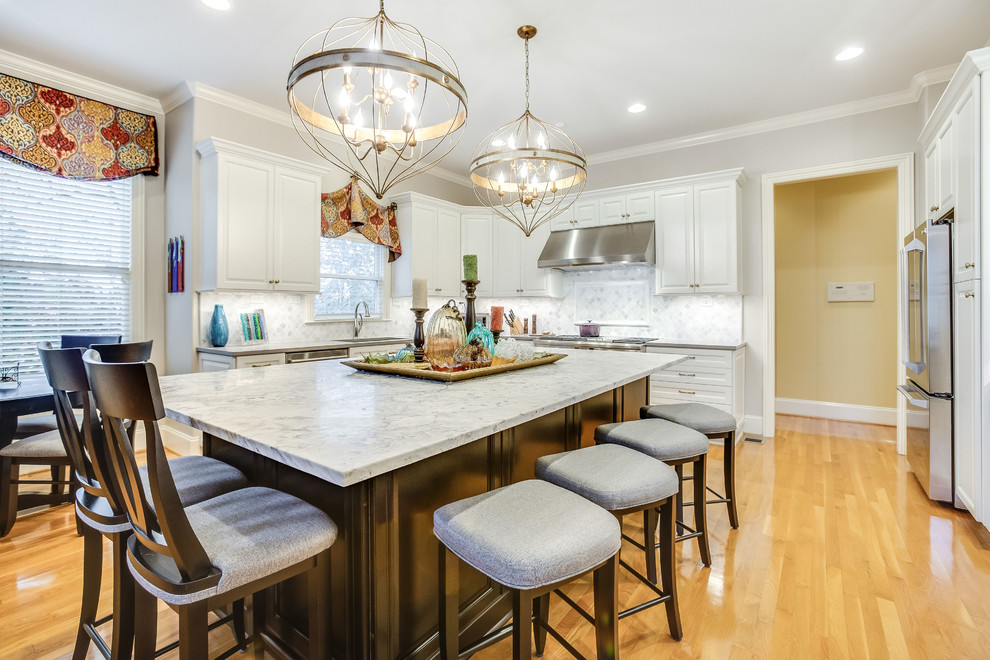 Example of a large transitional u-shaped light wood floor and yellow floor open concept kitchen design in Birmingham with raised-panel cabinets, white cabinets, marble countertops, white backsplash, marble backsplash, stainless steel appliances, an island and white countertops