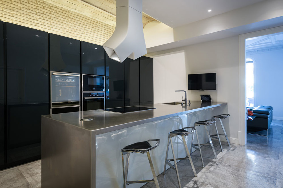 Photo of a large modern single-wall separate kitchen in Barcelona with a single-bowl sink, flat-panel cabinets, black cabinets, zinc benchtops, black appliances, porcelain floors, with island and grey floor.