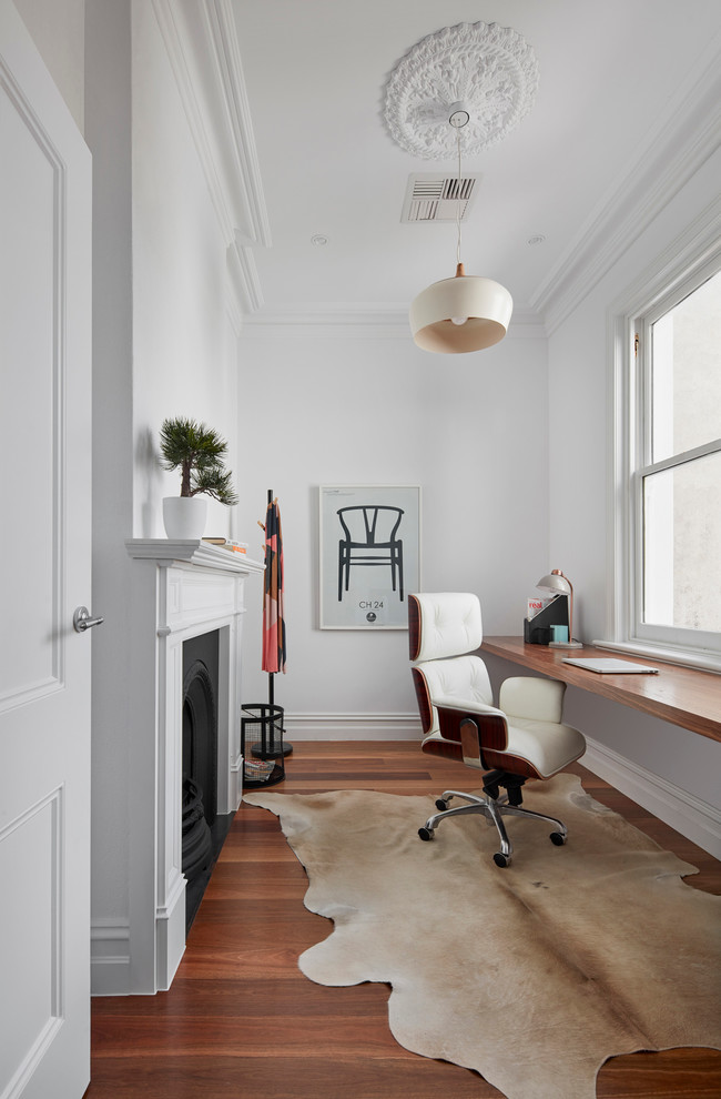Inspiration for a small contemporary home office in Melbourne with white walls, medium hardwood floors, a standard fireplace and a built-in desk.