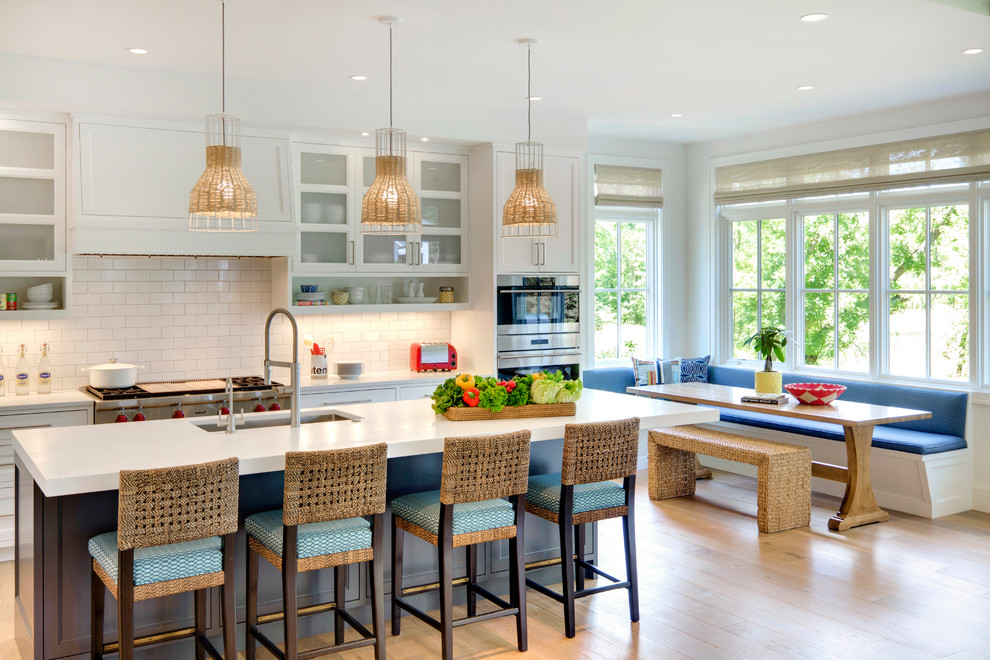 Photo of a beach style eat-in kitchen in Minneapolis with an undermount sink, shaker cabinets, white cabinets, white splashback, subway tile splashback, light hardwood floors and with island.