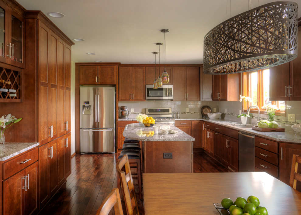 Large transitional l-shaped dark wood floor enclosed kitchen photo in Milwaukee with a drop-in sink, shaker cabinets, medium tone wood cabinets, granite countertops, white backsplash, porcelain backsplash, stainless steel appliances and an island