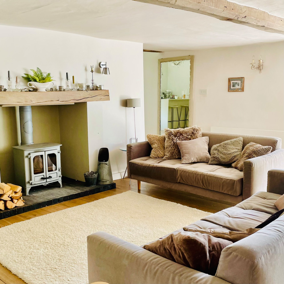 Photo of a mid-sized contemporary living room in Hampshire with white walls, medium hardwood floors, a wood stove and a wood fireplace surround.