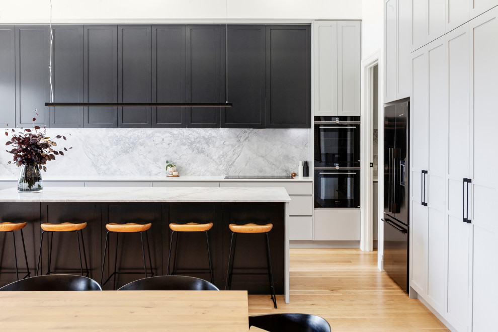 Inspiration for a large contemporary u-shaped open plan kitchen in Melbourne with a double-bowl sink, shaker cabinets, marble benchtops, grey splashback, marble splashback, black appliances, light hardwood floors, with island and grey benchtop.