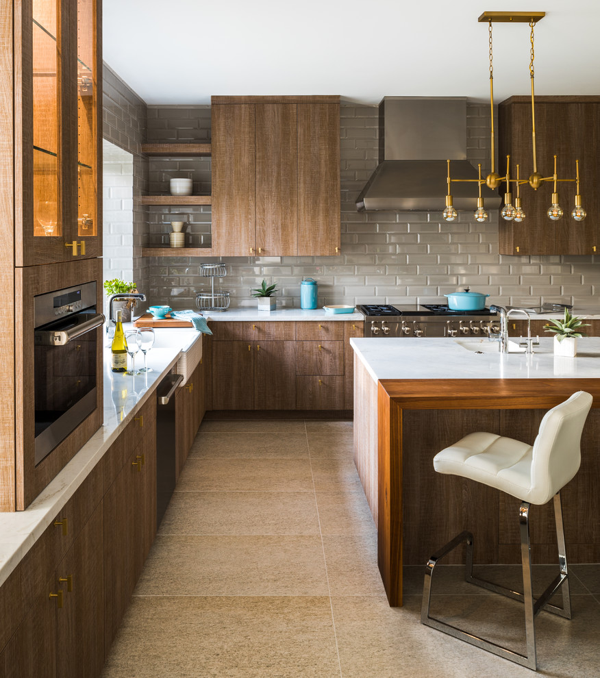 Photo of a contemporary l-shaped kitchen in Phoenix with a farmhouse sink, flat-panel cabinets, dark wood cabinets, grey splashback, subway tile splashback, stainless steel appliances, with island, beige floor and white benchtop.