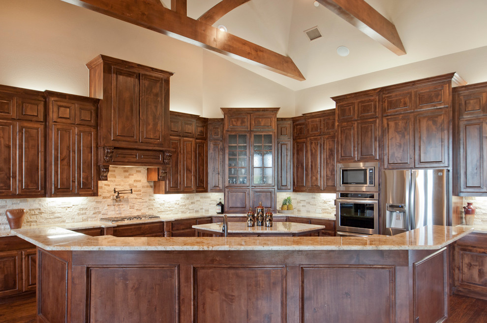 Example of a large transitional galley dark wood floor open concept kitchen design in Dallas with an undermount sink, raised-panel cabinets, medium tone wood cabinets, granite countertops, beige backsplash, stone tile backsplash, stainless steel appliances and an island