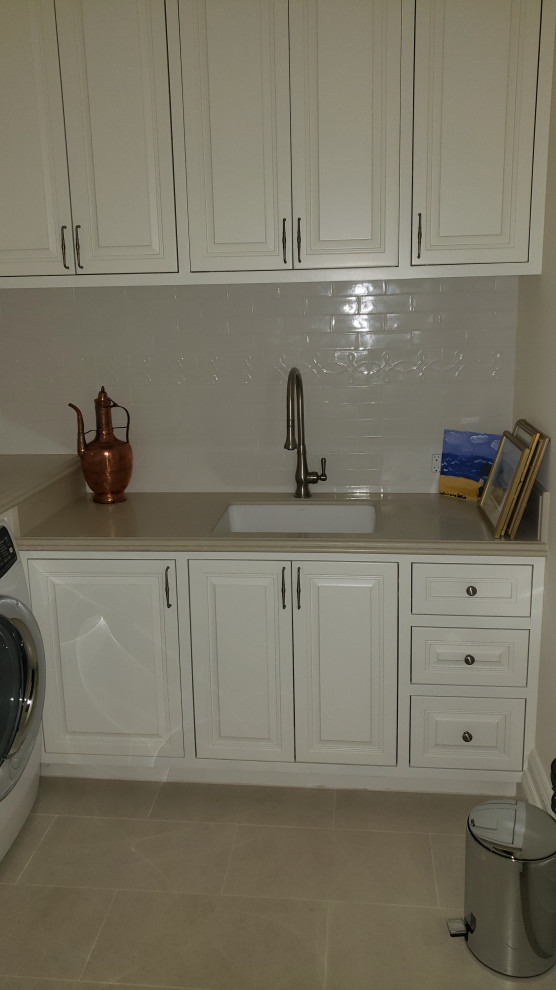 Dedicated laundry room - mid-sized traditional l-shaped dedicated laundry room idea in Orange County with an undermount sink, raised-panel cabinets, distressed cabinets, quartz countertops, an integrated washer/dryer and beige countertops