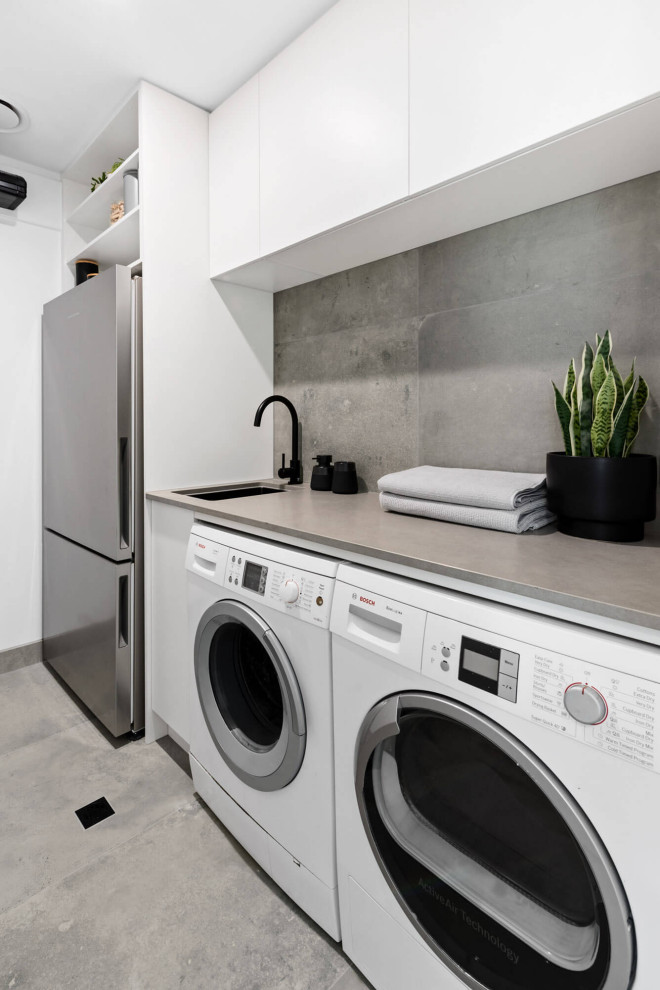 Design ideas for a medium sized contemporary single-wall utility room in Melbourne with a submerged sink, flat-panel cabinets, white cabinets, concrete worktops, grey splashback, cement tile splashback, white walls, concrete flooring, a side by side washer and dryer, grey floors and grey worktops.