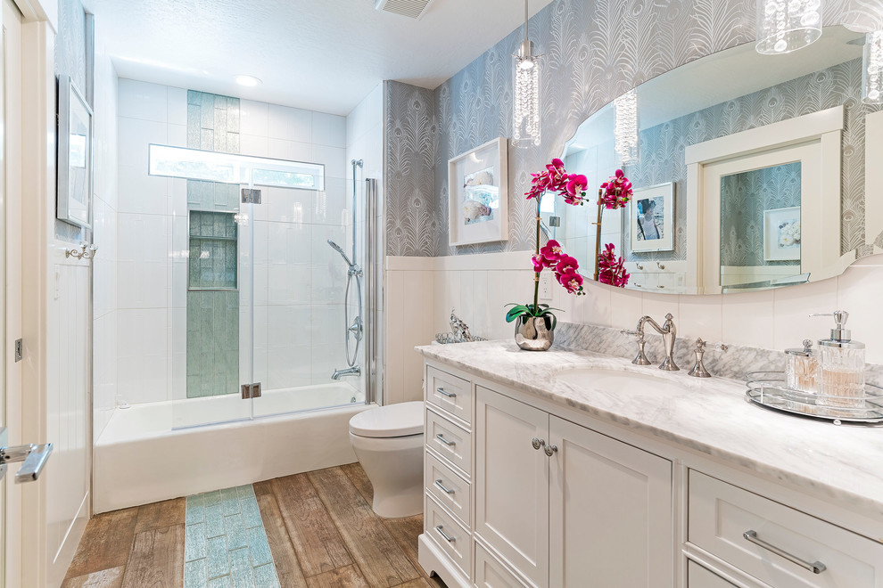 This is an example of a country 3/4 bathroom in Other with recessed-panel cabinets, white cabinets, an alcove tub, a shower/bathtub combo, green tile, white tile, grey walls, an undermount sink, brown floor, a hinged shower door and grey benchtops.