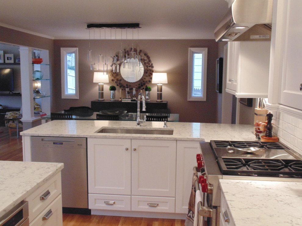 Large transitional u-shaped medium tone wood floor and brown floor eat-in kitchen photo with an undermount sink, recessed-panel cabinets, white cabinets, quartz countertops, white backsplash, subway tile backsplash, stainless steel appliances, an island and white countertops