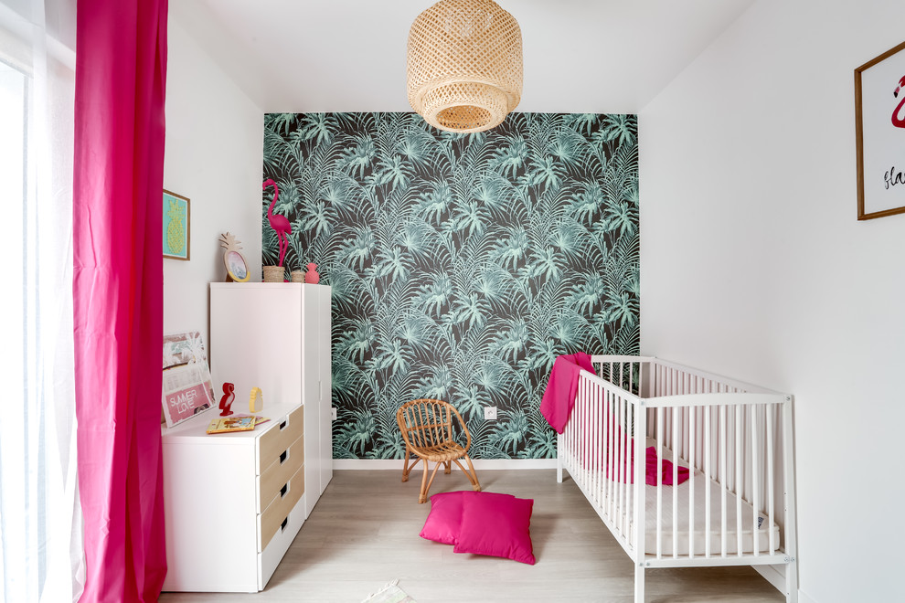 This is an example of a tropical nursery for girls in Paris with multi-coloured walls, light hardwood floors and beige floor.