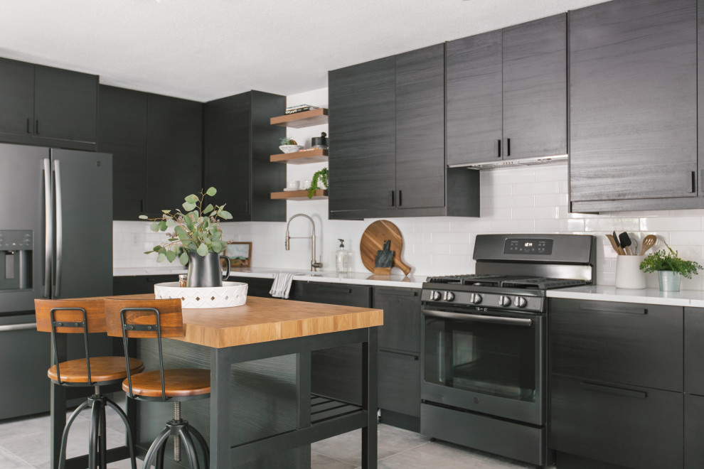 This is an example of a small scandinavian l-shaped kitchen in Tampa with a drop-in sink, flat-panel cabinets, black cabinets, quartz benchtops, white splashback, engineered quartz splashback, black appliances, ceramic floors, with island, grey floor and white benchtop.