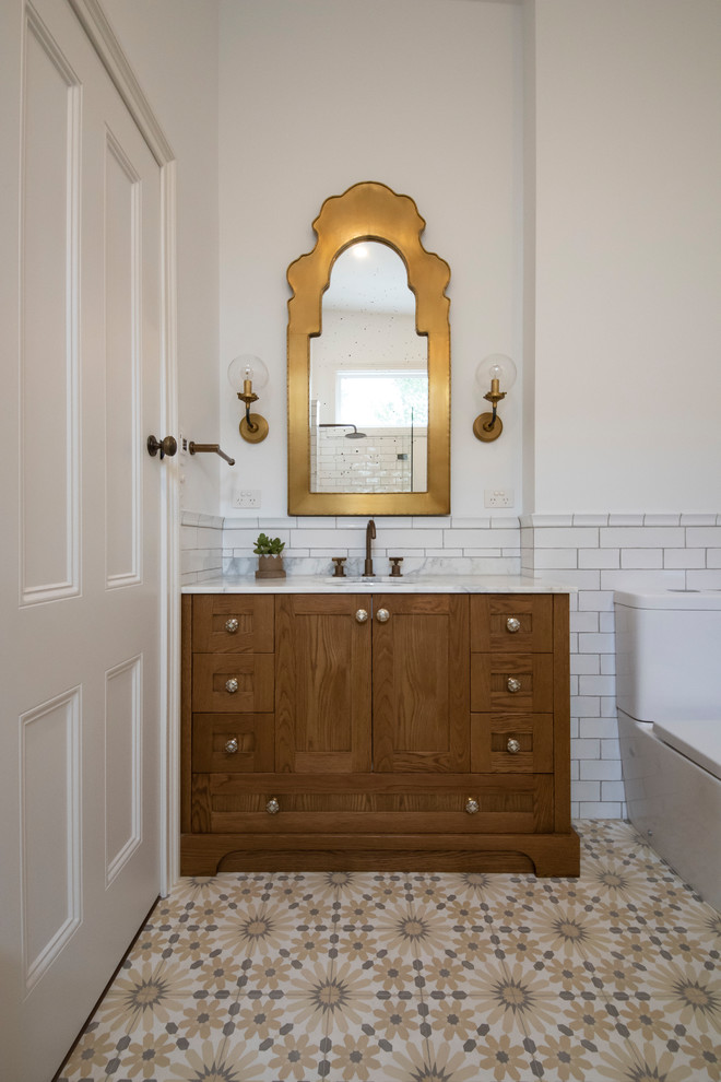 Large mediterranean master bathroom in Melbourne with furniture-like cabinets, medium wood cabinets, a claw-foot tub, white tile, ceramic tile, marble benchtops, white benchtops, a corner shower, a one-piece toilet, white walls, cement tiles, an undermount sink, yellow floor, an open shower, a single vanity and a built-in vanity.
