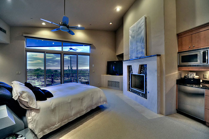 This is an example of an expansive contemporary master bedroom in Phoenix with beige walls, travertine floors, a standard fireplace, a tile fireplace surround and beige floor.