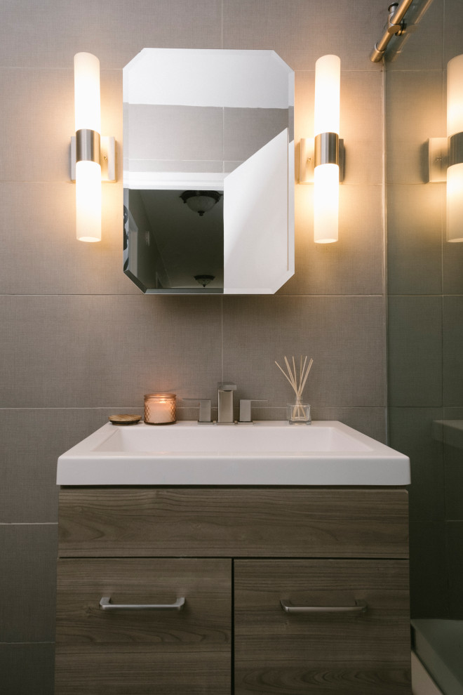 This is an example of a small classic bathroom in New York with flat-panel cabinets, medium wood cabinets, a built-in bath, a shower/bath combination, a one-piece toilet, grey tiles, porcelain tiles, grey walls, porcelain flooring, a console sink, quartz worktops, grey floors, a sliding door, white worktops, a single sink, a freestanding vanity unit and a vaulted ceiling.