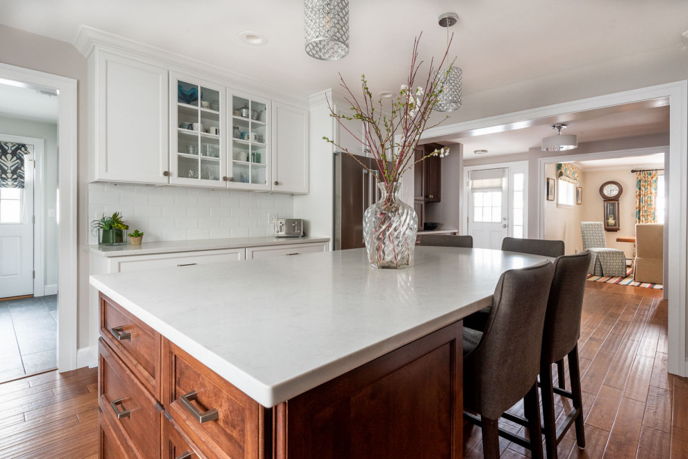 Large transitional l-shaped medium tone wood floor and brown floor eat-in kitchen photo in Boston with an undermount sink, shaker cabinets, white cabinets, quartz countertops, white backsplash, subway tile backsplash, stainless steel appliances, an island and white countertops