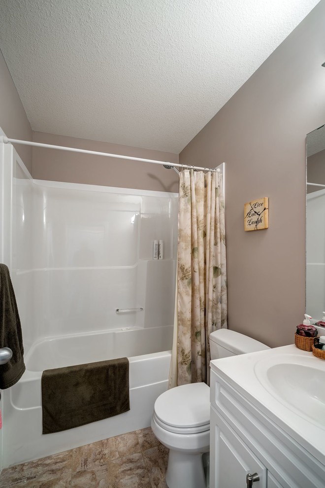 This is an example of a mid-sized modern kids bathroom in Vancouver with shaker cabinets, white cabinets, a shower/bathtub combo, a one-piece toilet, beige walls and a drop-in sink.