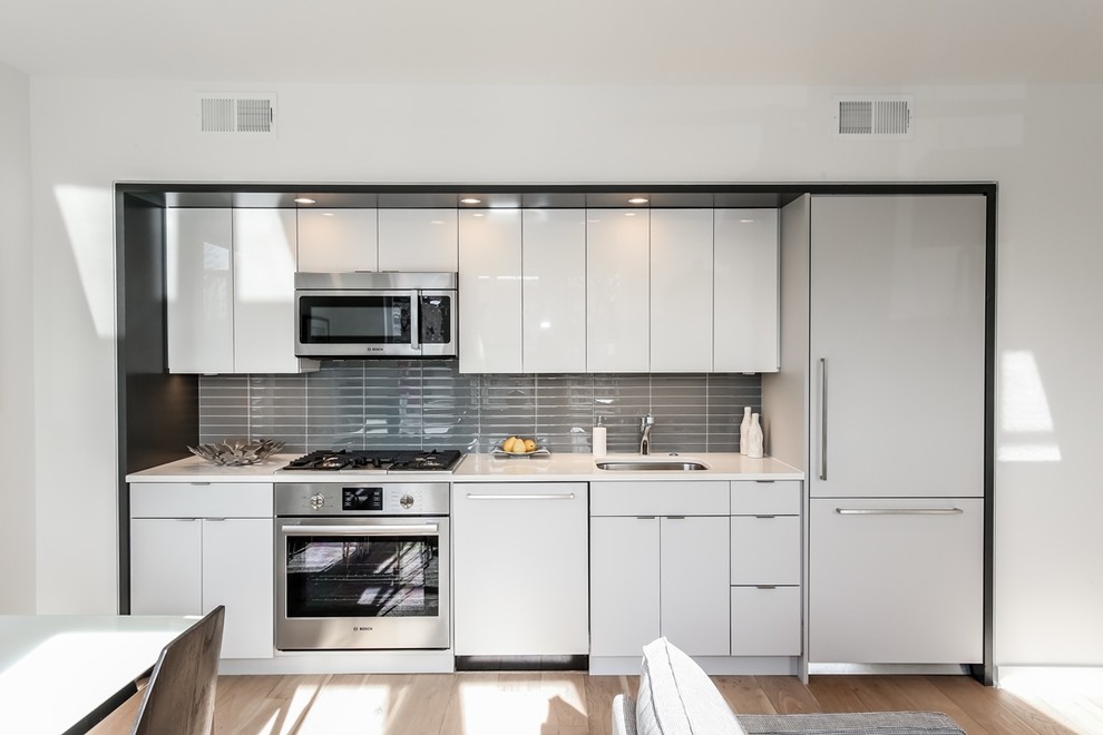 Inspiration for a small modern single-wall eat-in kitchen in DC Metro with a drop-in sink, flat-panel cabinets, quartz benchtops, grey splashback, ceramic splashback, panelled appliances, light hardwood floors, with island and white cabinets.