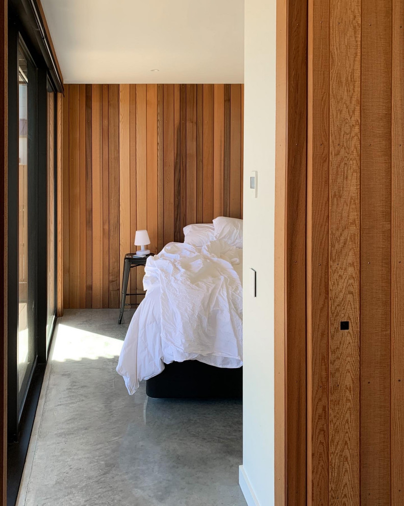 This is an example of a mid-sized contemporary guest bedroom in Auckland with brown walls, concrete floors, no fireplace, grey floor, recessed and decorative wall panelling.