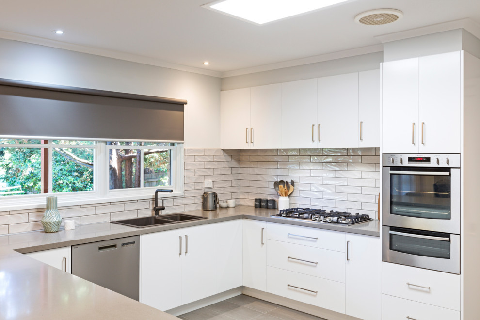 Inspiration for a mid-sized modern u-shaped eat-in kitchen in Melbourne with a double-bowl sink, flat-panel cabinets, white cabinets, quartz benchtops, white splashback, subway tile splashback, no island and grey benchtop.